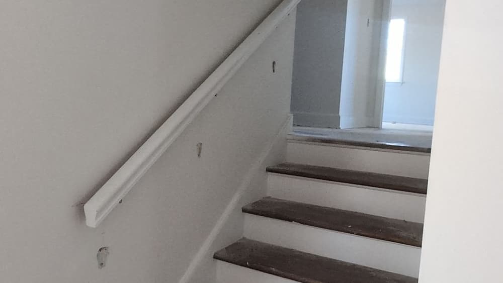 Staircase with new white risers, wood treads and a handrail part way through refinishing