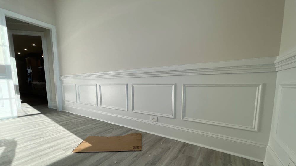 White wainscot panel trim installed along a hallway wall above light grey plank flooring