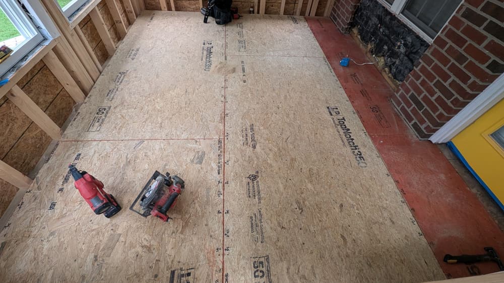 Subfloor sheathing laid across a rear porch slab with tools on the deck
