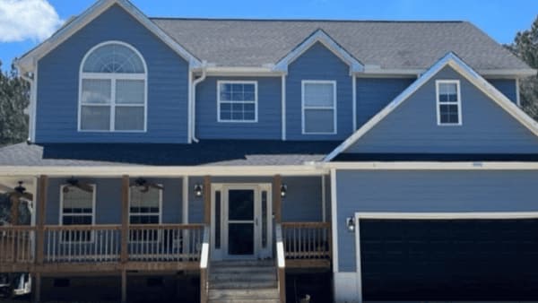 Blue siding two-story home exterior with a covered front porch, dark garage door and front steps