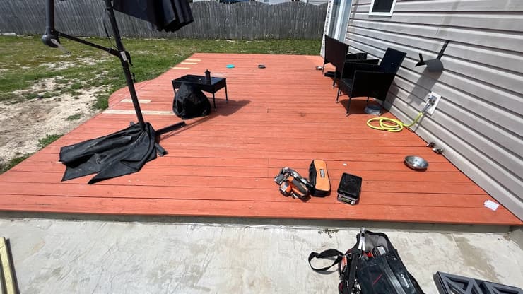 Freshly stained red deck behind a house with patio furniture and tools