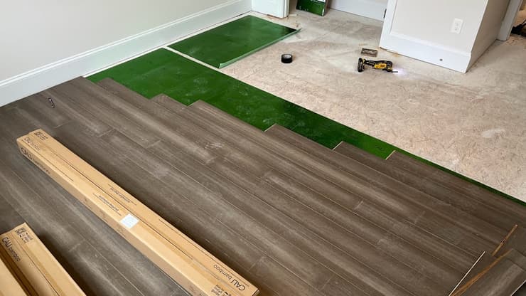 Wood-look plank flooring being installed over green underlayment with planks and a drill on the floor