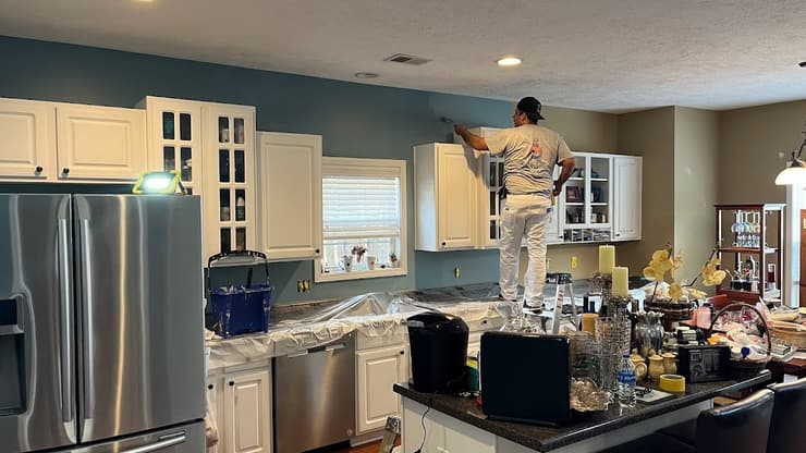 Painter on a ladder cutting in a kitchen ceiling with the counters covered below