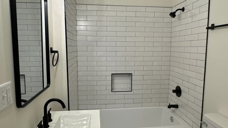 Bathroom with a white subway tile tub surround, black fixtures, wood vanity and framed mirror