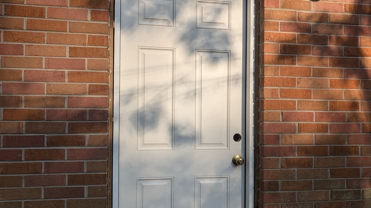 New white six panel exterior door installed in a brick wall with a light fixture