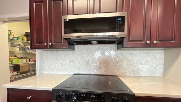 Kitchen with dark cherry cabinets, a herringbone tile backsplash and a black cooktop