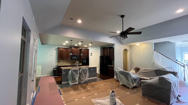 Open living and kitchen area with a ceiling fan and drop cloths on the floor mid project
