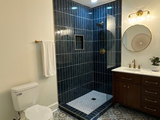 Bathroom with a dark blue tile shower, patterned floor tile, wood vanity and round mirror