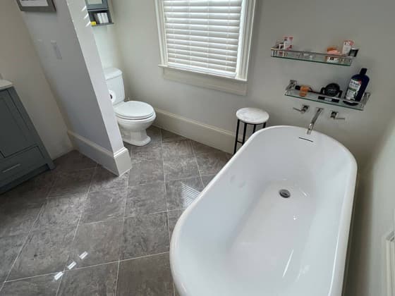 Bathroom with a freestanding oval tub, grey tile floor, toilet and window