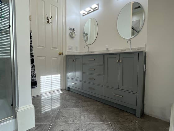 Grey double vanity bathroom with two round mirrors, wall sconces and tile floor