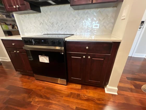 Dark cherry kitchen cabinets and a range above a wood floor