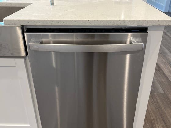 Stainless dishwasher installed in a white cabinet run beside a quartz countertop
