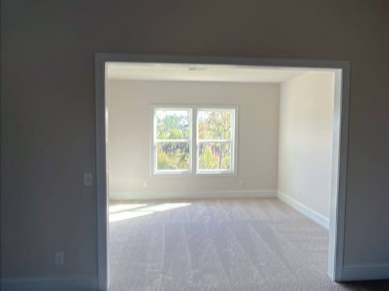 Empty room with fresh grey carpet and a wide cased opening to a bright window