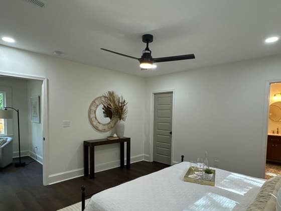 Bedroom with a ceiling fan, made bed, console table and round mirror