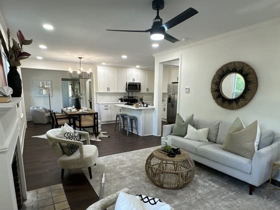 Open living room with a ceiling fan, white sofa, round mirror and a view through to the kitchen