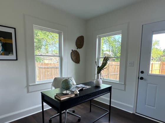 Home office with a black desk between two windows over dark wood floors