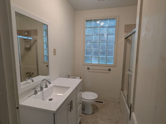 Small bathroom with a white vanity, toilet and a glass block window