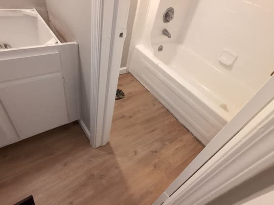 Bathroom under renovation with a white tub and shower, new flooring and an open doorway