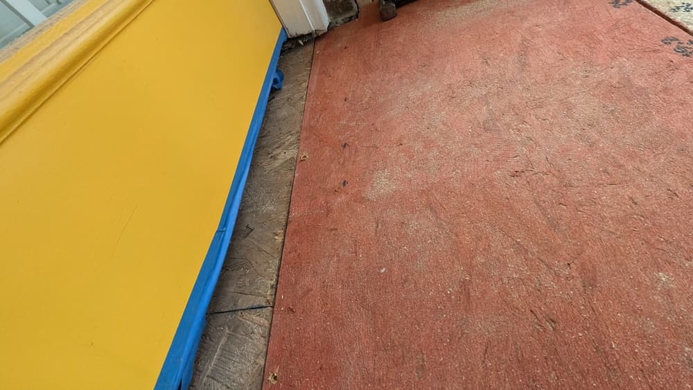 Concrete subfloor stripped of its finish flooring beside a yellow wall with blue tape