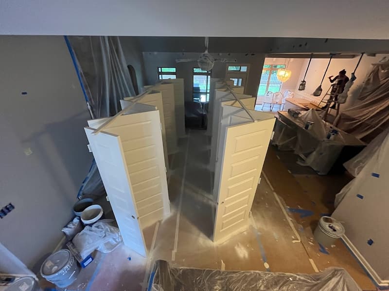 Interior under renovation with plastic sheeting and stacked new cabinet doors on a covered floor