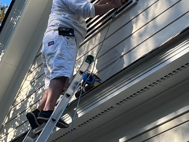 Painter on a ladder working along the exterior siding of a home