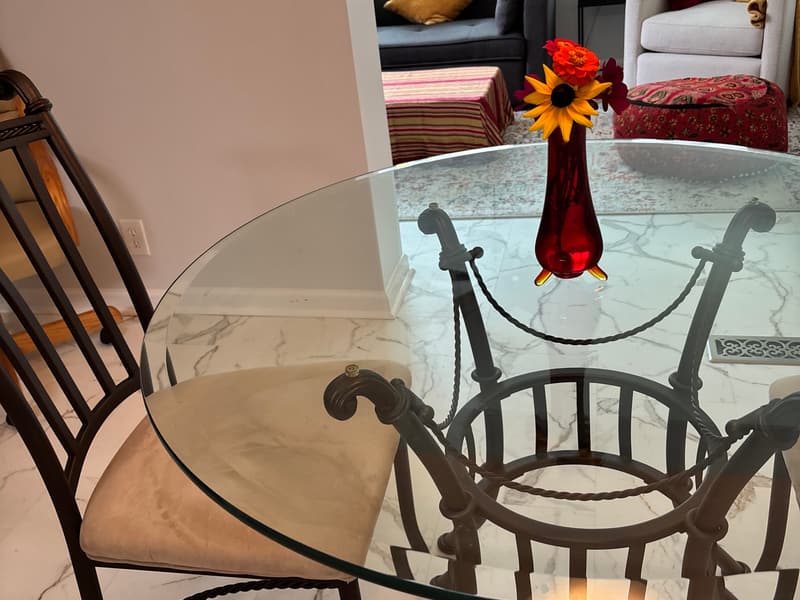 Glass-top dining table with wrought iron chairs and a flower vase in a finished room