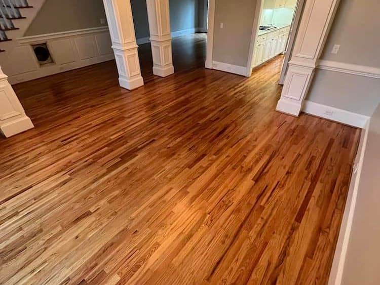 Refinished hardwood flooring in an empty room with white trim and columns